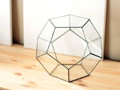 a glass geometric object sitting on top of a wooden table next to a white wall