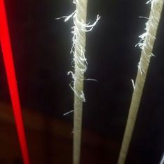 two sticks with some white yarn on them and red string attached to them in front of a black background