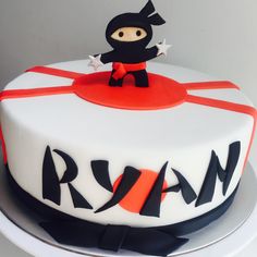 a white cake with red and black decorations on it's sides, topped with an orange ribbon