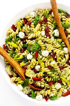 a white bowl filled with pasta salad and two wooden utensils in front of it