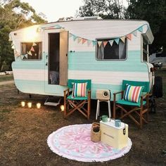 an rv is parked in the grass with two chairs and a table next to it