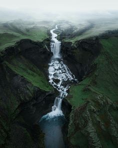 an aerial view of a waterfall in the middle of a green valley with water running down it