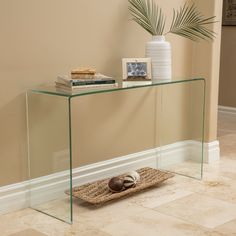 a glass console table with a basket on the floor next to it and a potted plant