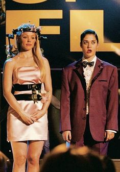 two people standing on stage with one person wearing a dress and the other in a tuxedo