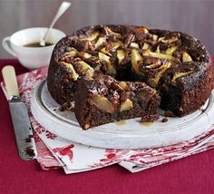 a chocolate cake with nuts on top sitting on a plate next to a bowl and spoon