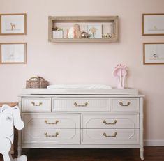 a baby's room with pink walls, white dressers and pictures on the wall