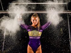 a woman in a purple and gold leotard posing for the camera with white powder behind her