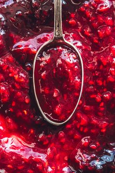 a spoon is full of cranberry sauce in a pot with water droplets on it