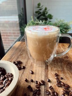 a cup of coffee sitting on top of a wooden table next to some coffee beans