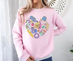 a woman wearing a pink sweatshirt with cartoon drawings on it, standing in front of a white wall