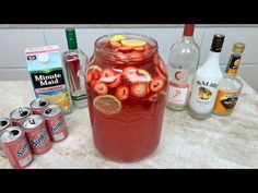 a mason jar filled with sliced strawberries and lemons next to bottles of alcohol