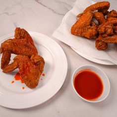 two plates filled with fried chicken wings next to a cup of sauce