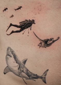 a man's chest with shark and scuba diver tattoos on his back, while sharks swim in the water behind him