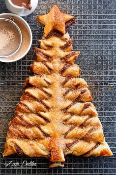 a pastry shaped like a christmas tree on a cooling rack next to two cups of coffee