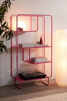 a pink shelving unit next to a lamp and a record player on a rug