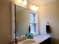 a bathroom with two sinks and a large mirror on the wall above it is lit by three lights