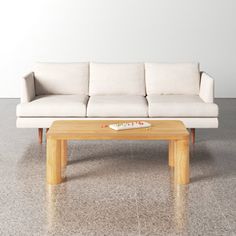 a white couch sitting next to a wooden table on top of a cement floor in front of a white wall