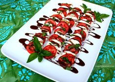 a white plate topped with sliced tomatoes covered in chocolate sauce and green leafy garnish