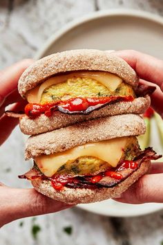 a person holding a sandwich in their hand with cheese and sauce on it, next to a plate