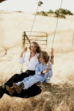 a woman and child sitting on a swing in the middle of an open field with hay