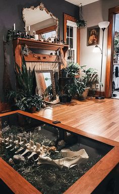 a living room filled with lots of plants next to a fire place in the middle of a wooden floor