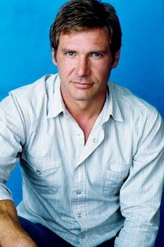 a man sitting down in front of a blue background wearing a white shirt and jeans