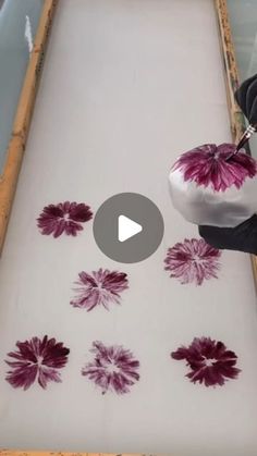 someone is painting flowers on the floor with white and purple paint in front of them