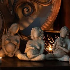 three little statues sitting next to a lit candle