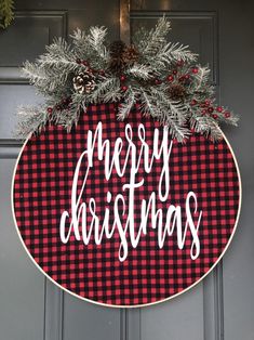 a red and black plaid christmas door hanger with pine cones, evergreen leaves and the words merry christmas on it