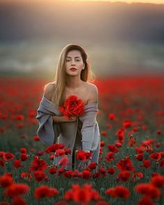 a woman standing in a field with red flowers on her chest and arms around her body