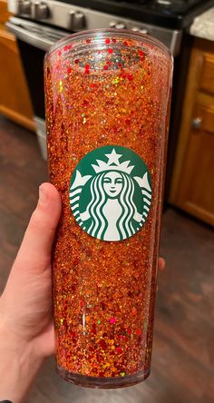 a person holding up a starbucks cup filled with red sprinkles and gold flakes