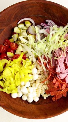 a wooden bowl filled with different types of vegetables and meats on top of each other