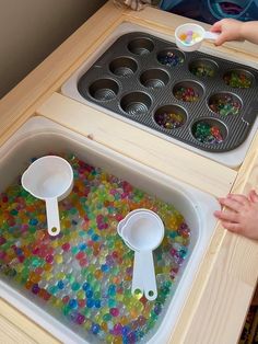 two children are playing with colored beads in an ice cream mold tray and spoons