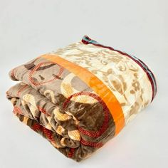 three blankets folded on top of each other in different colors and patterns, one with an orange stripe down the middle