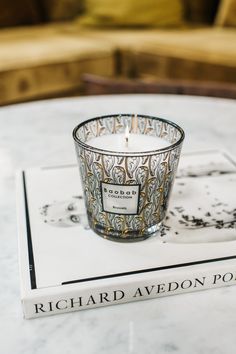 a glass candle sitting on top of a white table next to a black and gold book