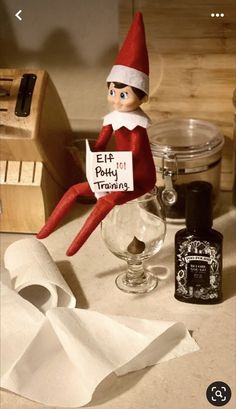 an elf sitting on top of a counter next to a bottle of alcohol and napkins