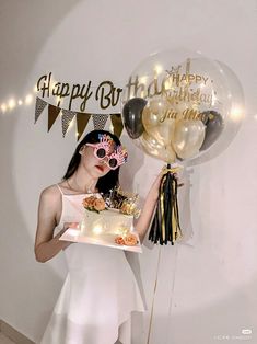 a woman holding a birthday cake and balloons