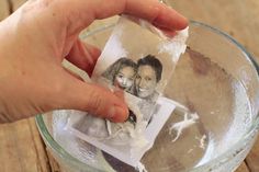 a hand holding an old photo in a glass with ice on the table next to it