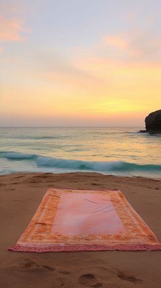 an orange and white blanket laying on top of a sandy beach next to the ocean