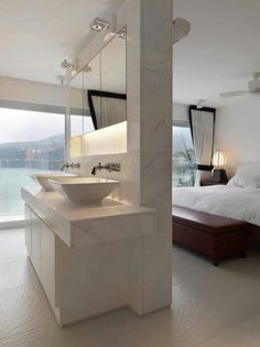 a bedroom with a bed, sink and large window looking out onto the water in front of it