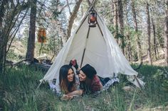 two young women laying in the grass near a teepee with lights hanging from it