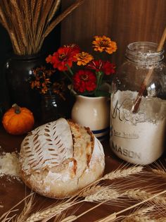 bread, flour and flowers on a table in front of some jars with dried plants