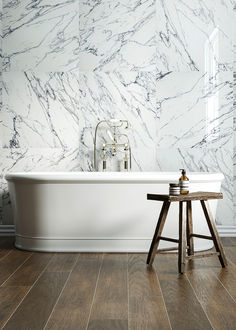 a white bath tub sitting on top of a wooden floor next to a table and stool