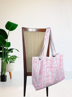 a pink and white bag sitting on top of a chair next to a potted plant