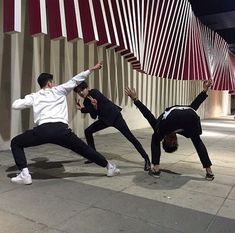 three young men are doing yoga on the sidewalk at night, with their hands in the air