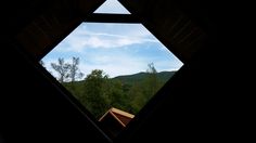 an open window showing the view of trees and mountains from inside a cabin in the woods