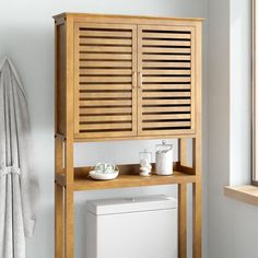 a wooden cabinet next to a white toilet in a room with towels on the wall