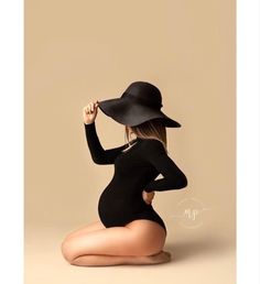 a woman in a black bodysuit and hat sitting on the ground