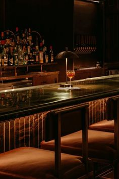 an empty bar with stools and bottles on the back wall, in a dimly lit room