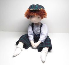 a doll sitting on the floor wearing a hat and plaid shirt with suspenders,